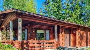 A rustic log cabin with a porch, stone foundation, and a forest backdrop.
