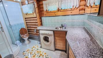 A compact bathroom with a wooden cabin-style design, including a toilet, washing machine, and sink.