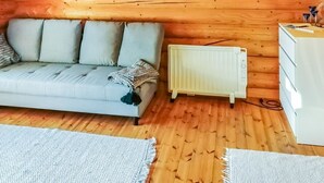 Een gezellige kamer in een houten blokhut met een lichtgrijze bank, een witte radiator en een witte dressoir.