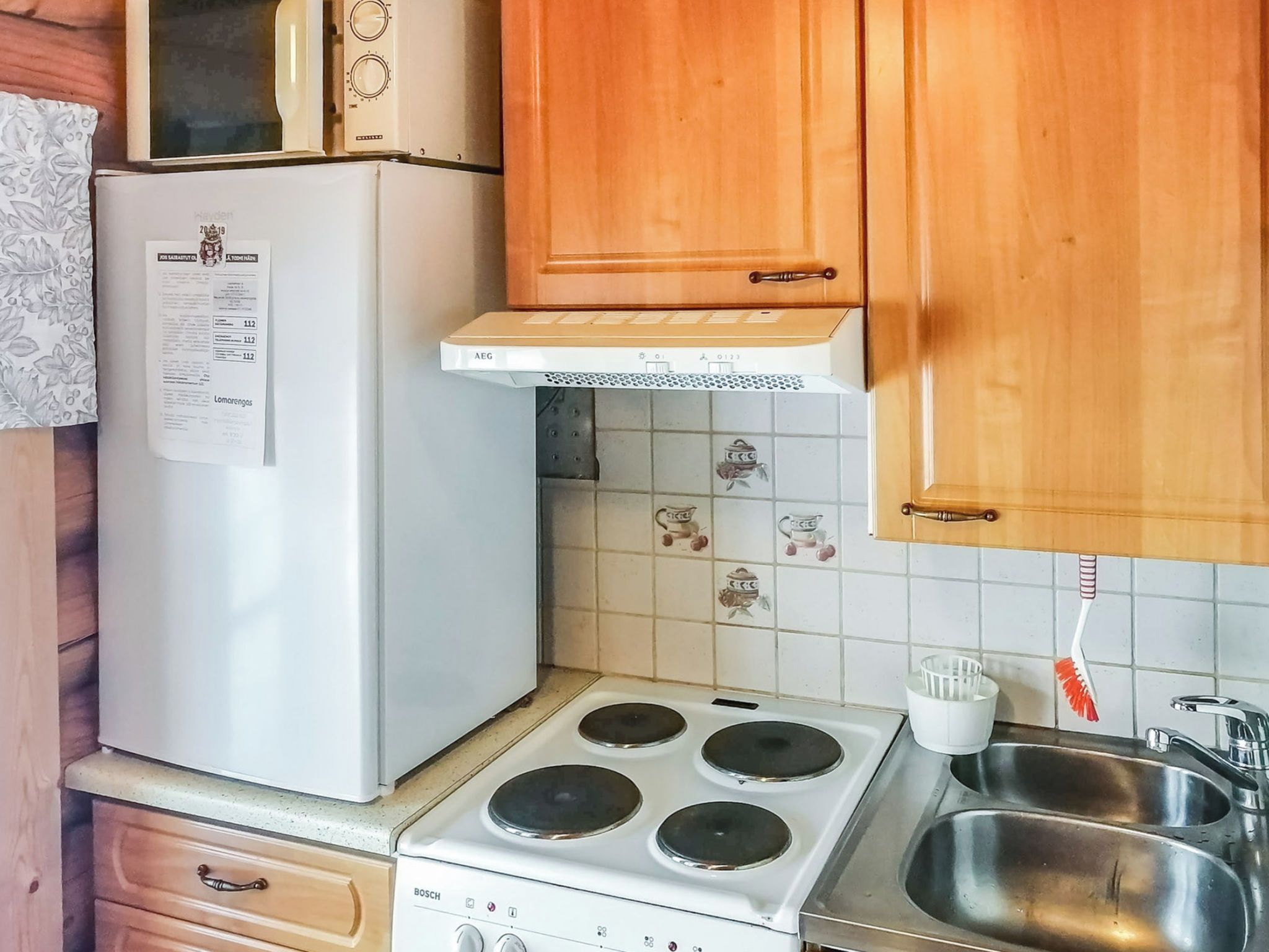 Et lille køkken med et hvidt køleskab, en Bosch komfur, træskabe og et flisebeklædt bagpanel.