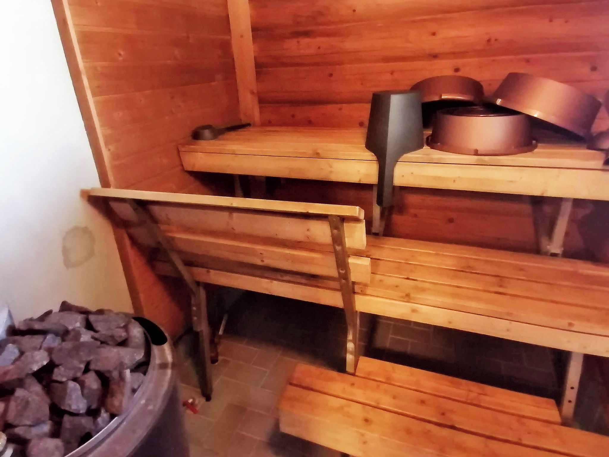 Una sauna in legno con panche e un contenitore metallico pieno di pietre.