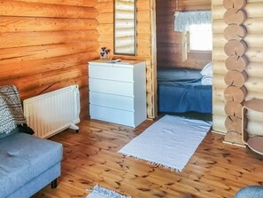 A log cabin interior with a sofa, a white dresser, a bed, and a window with a lace curtain. - Sillankorva by Interhome (Lapinlahti)