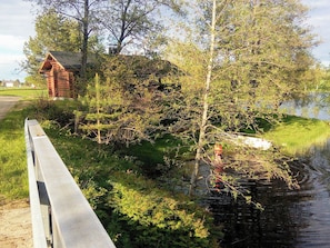 Uitzicht op een rivier met een houten brug, een klein rood gebouw en weelderige begroeiing.