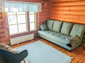 A cozy log cabin interior with a sofa, a chair, and a window with lace curtains.