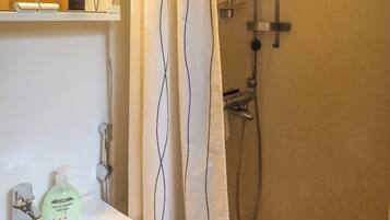 A bathroom with a shower, a sink, and a soap dispenser.
