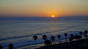 Un coucher de soleil sur l’océan, avec des palmiers et une plage au premier plan.