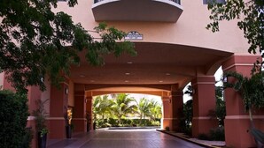 Entrada d'hotel amb un passadís cobert, palmeres i un senyal que indica un temps de desembre de 10 minuts.