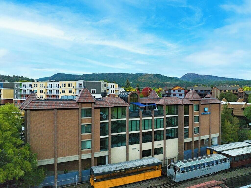 Un edificio de varios pisos con estilo arquitectónico moderno, que combina fachadas de ladrillo y vidrio, y un tren que pasa en primer plano.