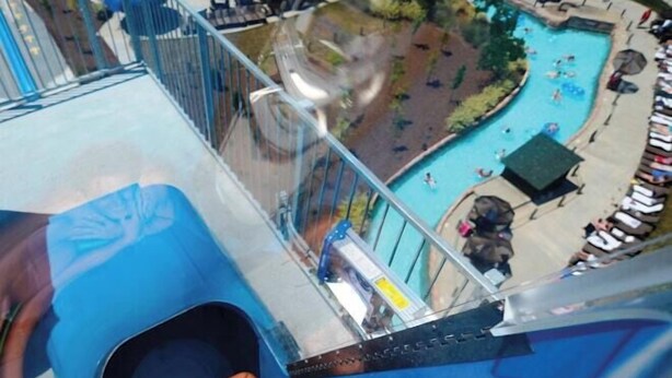 Una persona se desliza por un tobogán de agua azul con una piscina de fondo.