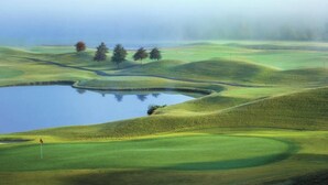 Un campo de golf con onduladas colinas verdes, un estanque y una bandera.