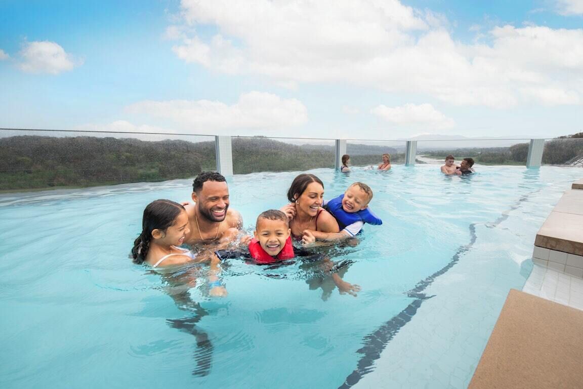 Une piscine où l’on voit des personnes, entourée d’un paysage boisé.