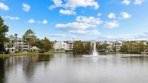 A tranquil lake with a fountain, surrounded by multi-story buildings with balconies and a clear sky. - All Suite Resort near Old Town Amusement Park and Disney World (Kissimmee)