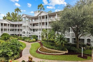 A multi-story hotel with a central courtyard, balconies, and lush landscaping. - All Suite Resort near Old Town Amusement Park and Disney World (Kissimmee)