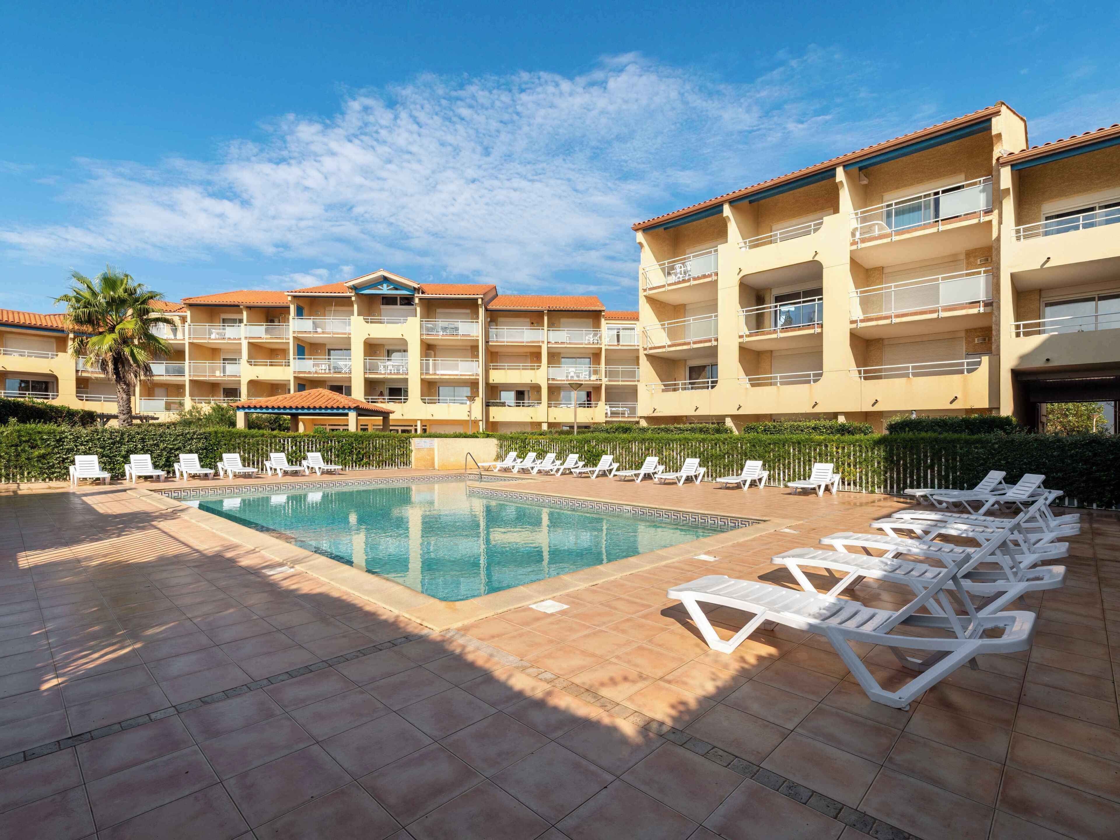 Un hotel con piscina, lettini e una palma.