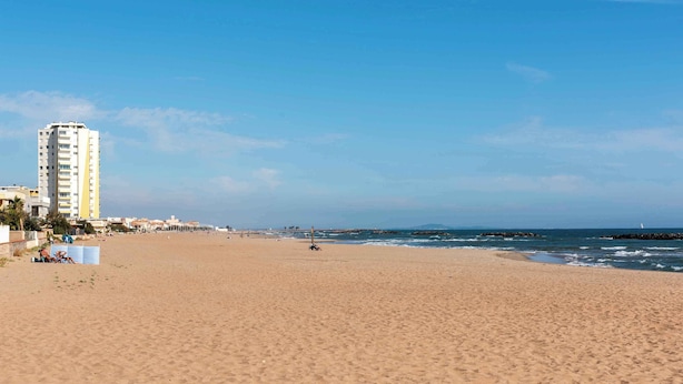 Ein weiter Sandstrand mit einem hohen Gebäude links und einem klaren, blauen Himmel.