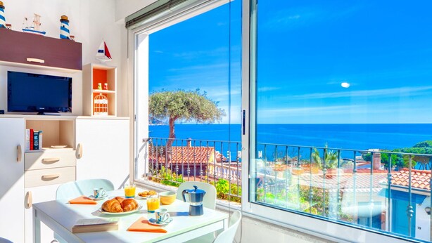 Ein Balkon mit Frühstückstisch, Fernseher und Blick aufs Meer.