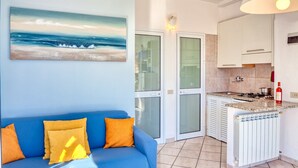 Ein Zimmer mit einem blauen Sofa, einer Küche mit Gasherd und einer Glastür, die in einen anderen Raum führt.