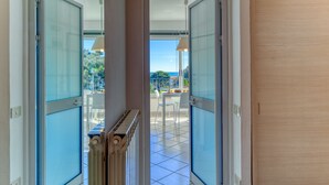 Blick durch eine Glastür auf einen Balkon mit Fliesenboden und einem Tisch mit Stühlen.