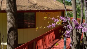 A red staircase leading to a yellow building with a brown roof, surrounded by trees with pink blossoms.