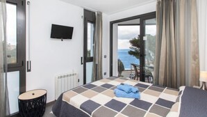 A bedroom with a large bed, a TV, a view of the sea, and a balcony.