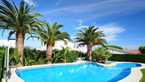 A swimming pool surrounded by palm trees and a white building with a red roof.