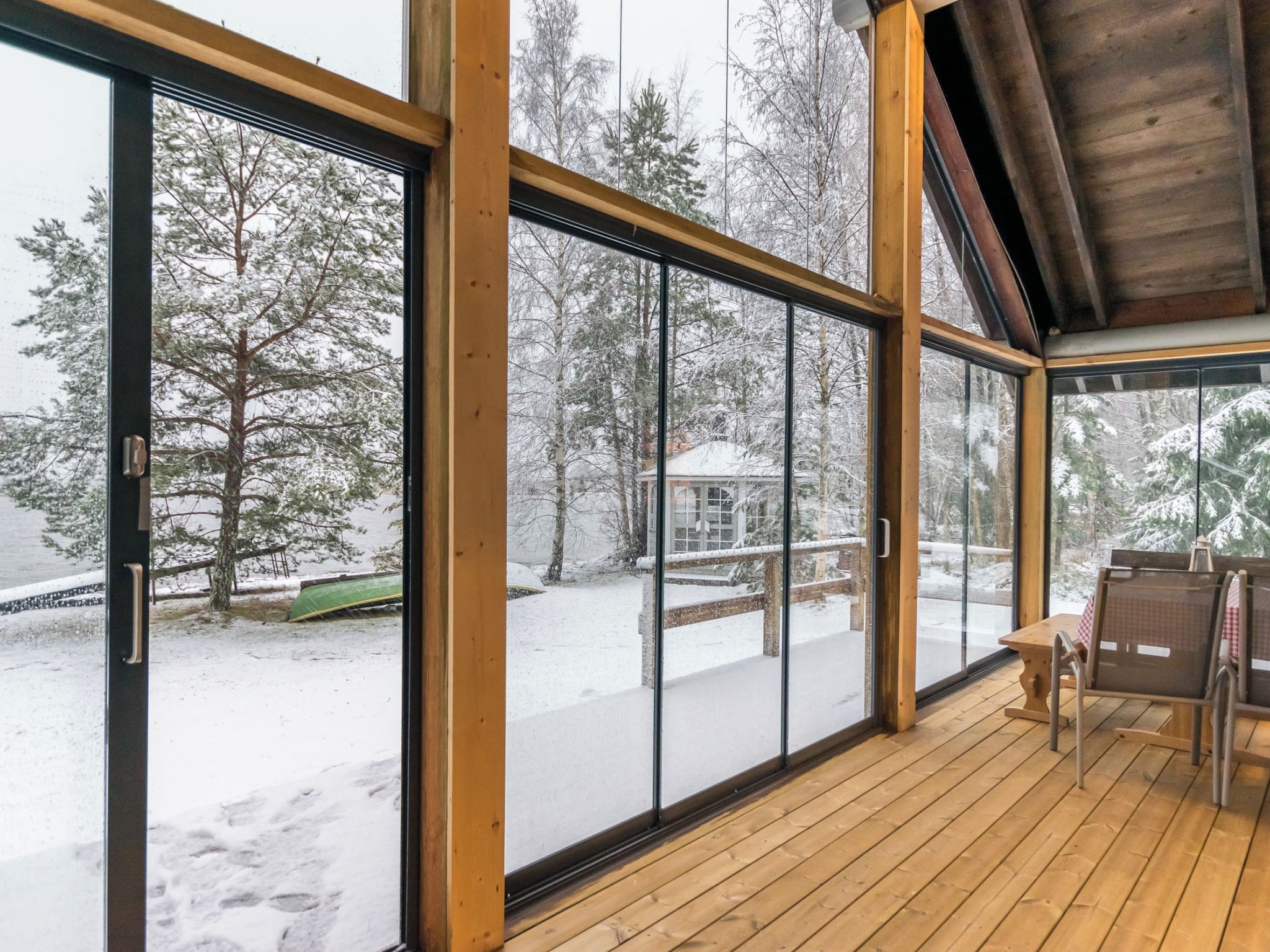 A spacious room with large glass doors leading to a snowy outdoor area, wooden flooring, and a bench.