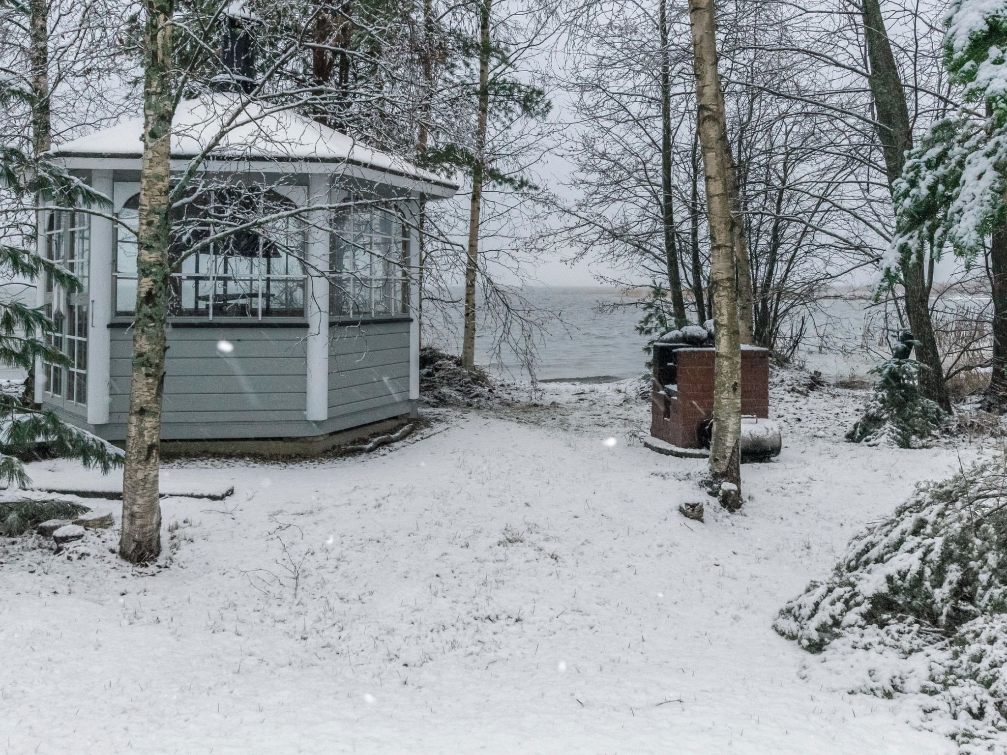 A cabin with a small porch, surrounded by snow-covered trees and a body of water in the background.