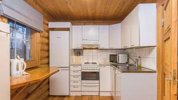 A compact kitchen with wooden walls, a built-in stove, a microwave, and a refrigerator.