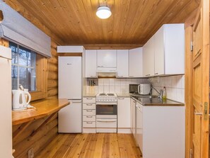 A compact kitchen with wooden walls, a built-in stove, a microwave, and a refrigerator.