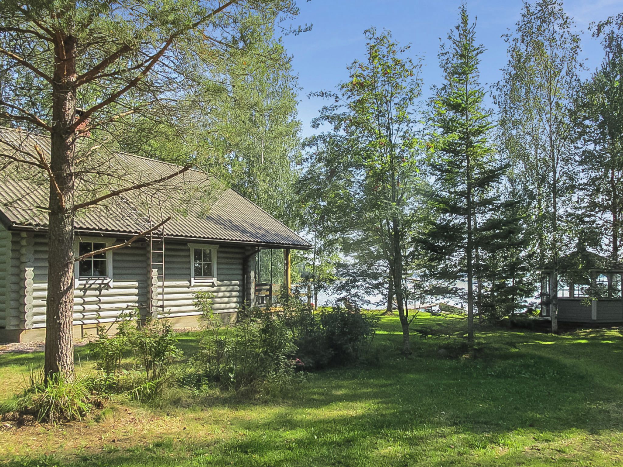 A log cabin with a metal roof, surrounded by a grassy area and trees.