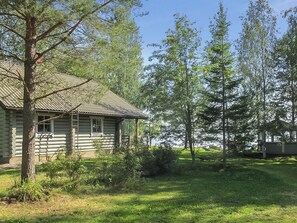 A log cabin with a metal roof, surrounded by a grassy area and trees.