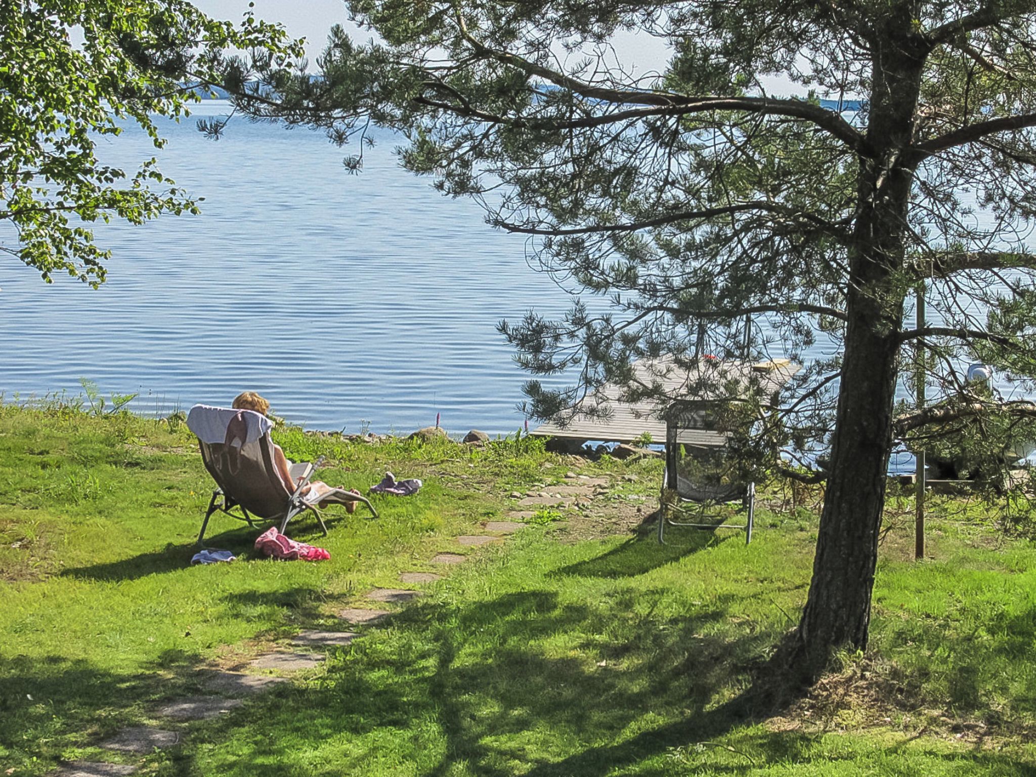 Kaunis paikka järven rannalla, jossa on tuoli ja riippumatto puun alla, puiset terassilankut ja esteetön näkymä vedelle.