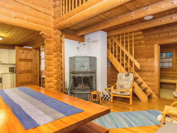 Interior de una cabaña de troncos con una mesa de comedor de madera, chimenea, escalera y zona de cocina.