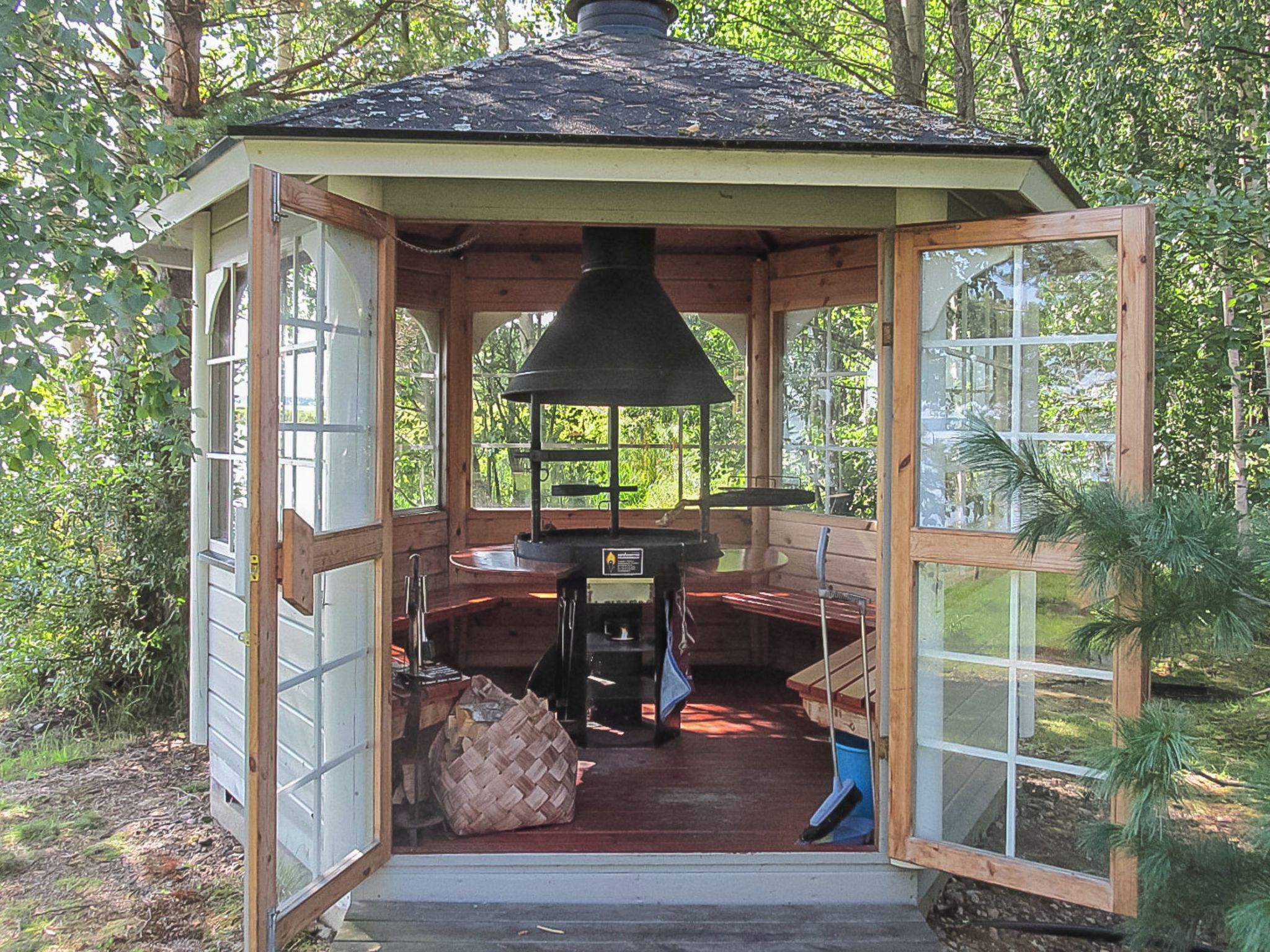 A wooden gazebo with a chimney, a table, and a bench.