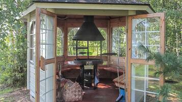 A wooden gazebo with a chimney, a table, and a bench.