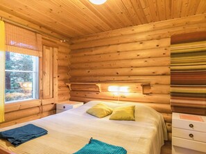 A wooden cabin room with a bed, bedside tables, and a window.
