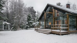 Una cabaña con fachada de vidrio, terraza de madera y un paisaje cubierto de nieve.