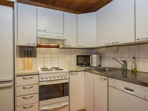 Una cocina con gabinetes blancos, estufa a gas, microondas y pileta.