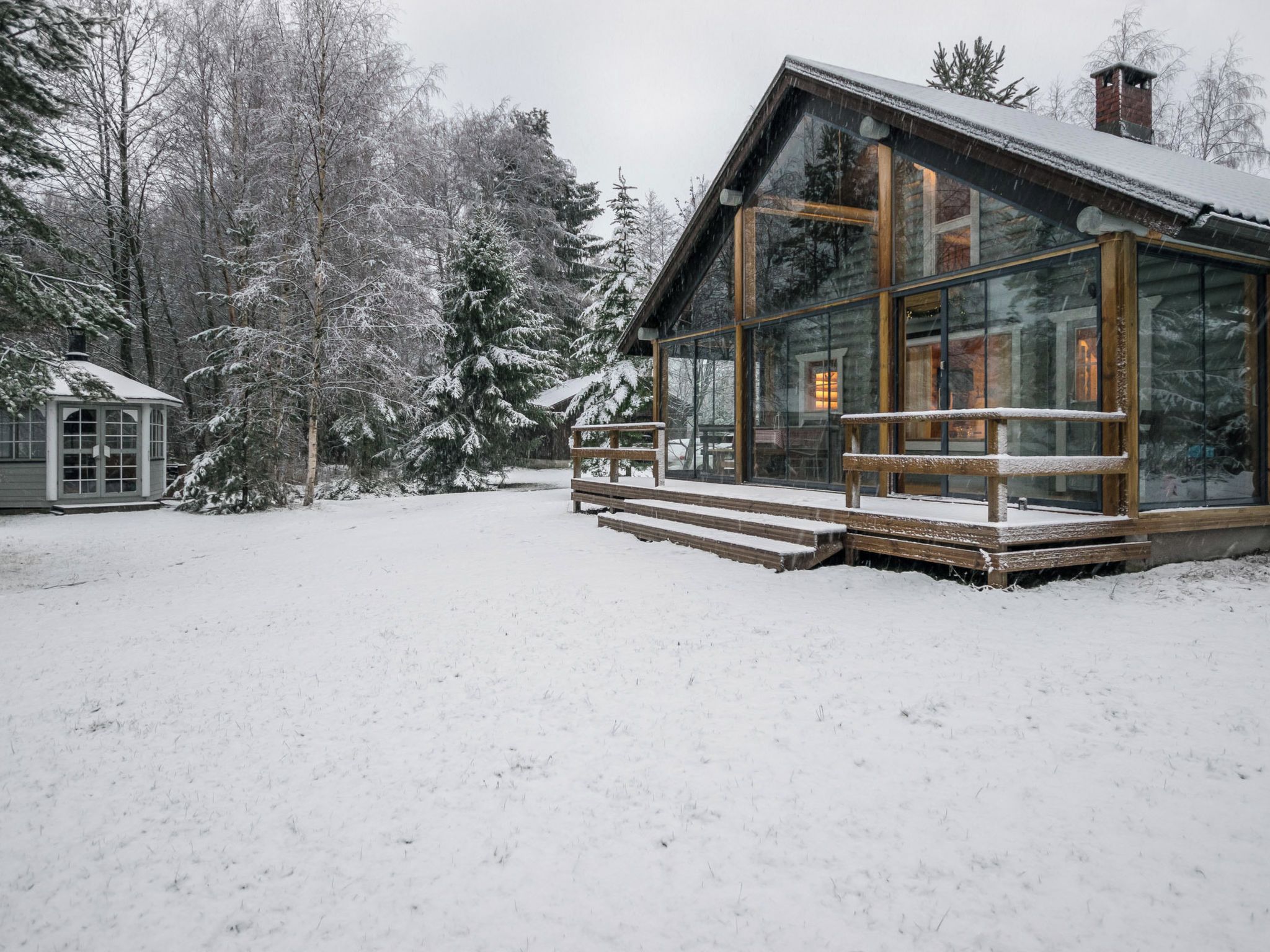 A wooden cabin with a glass extension, surrounded by snow-covered trees.