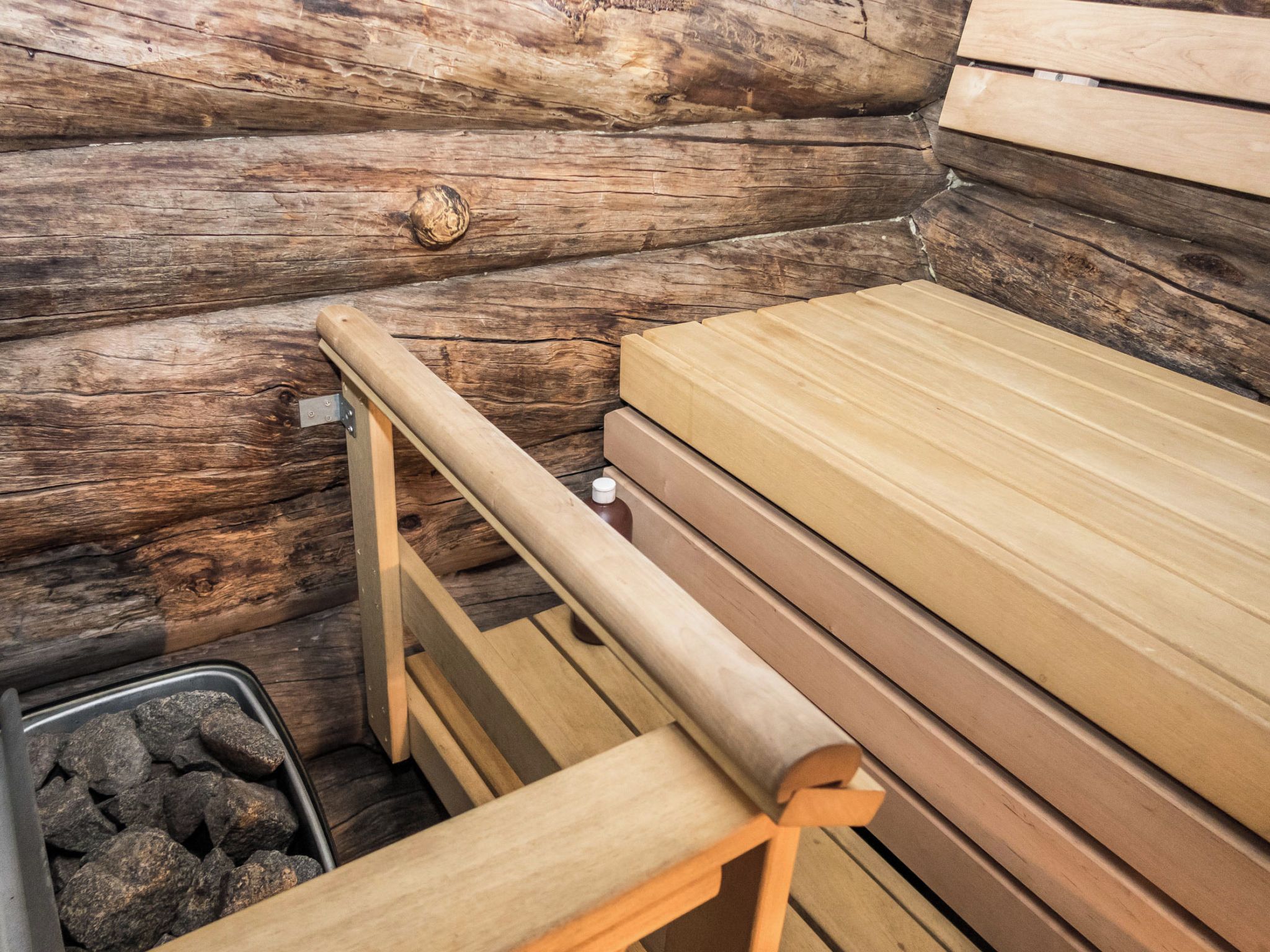 A sauna with wooden benches and a metal frame, set against a log wall.