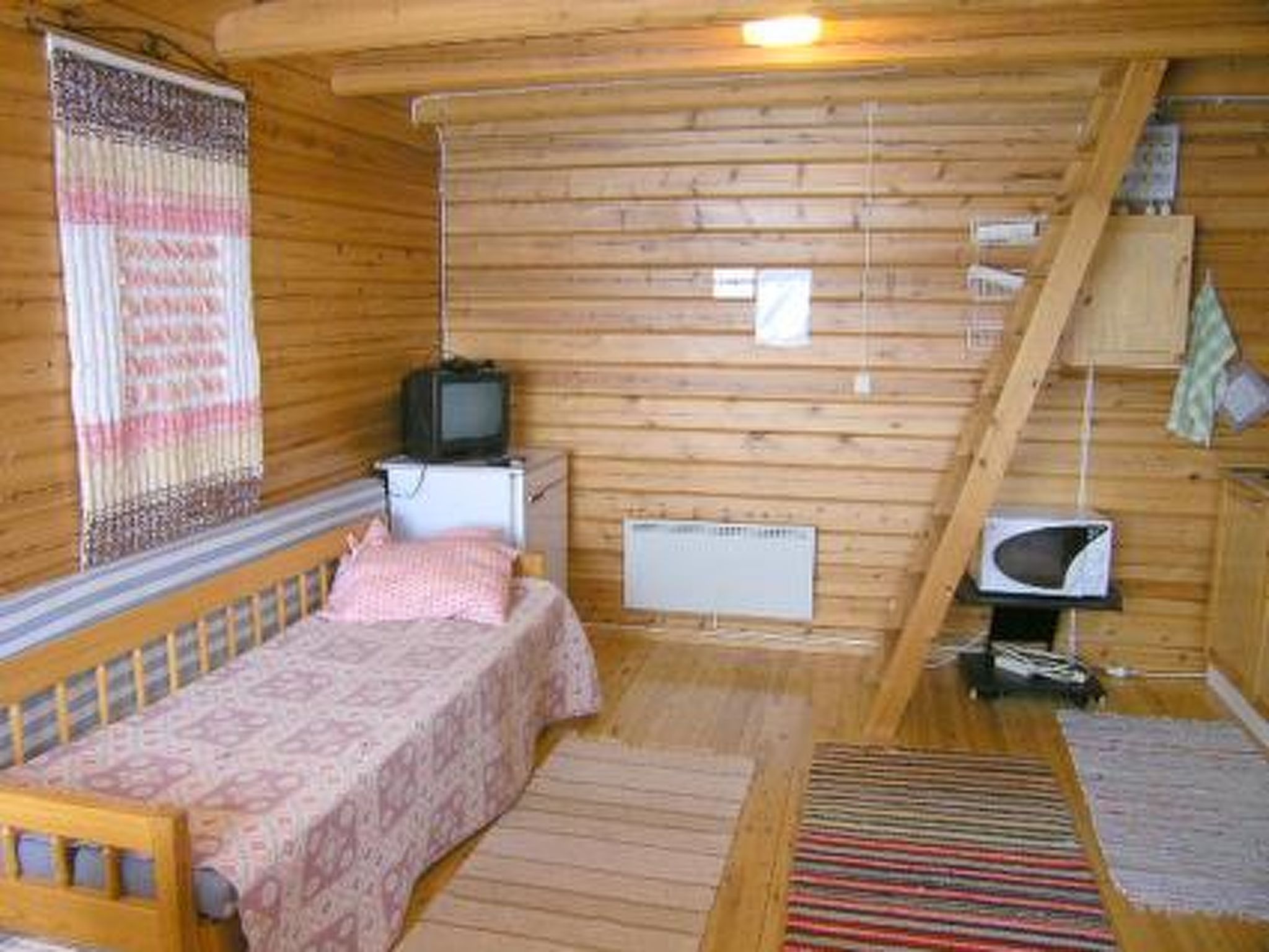 Een kleine houten kamer met een enkel bed, een televisie, een klein tafeltje en een magnetron.