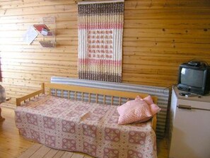 A small, cozy room with a wooden floor, a bed with a patterned bedspread, a television on a dresser, and a wall-mounted curtain. - Kallela by Interhome (Taivalkoski)