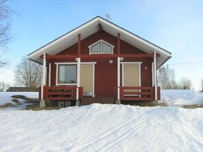 Une maison en bois rouge, avec un toit à pignon, deux fenêtres et un porche à l’avant.