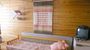 A small, cozy room with a wooden floor, a bed with a patterned bedspread, a television on a dresser, and a wall-mounted curtain.