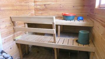 A small wooden cabin with a bench, a blue bucket, and a red container on a shelf.