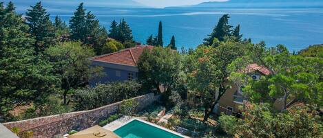 A pool area with two umbrellas, a stone wall, and a view of the sea and mountains.