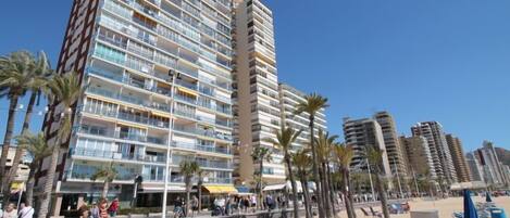 A beachfront hotel with multiple floors, balconies, and a sandy beach area with sun loungers.
