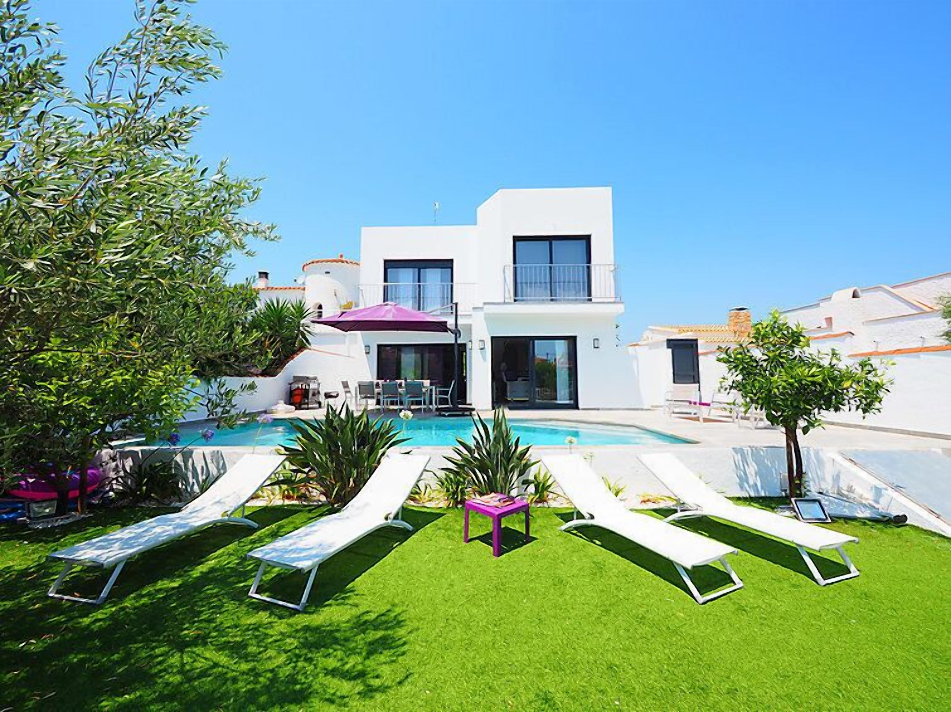 A modern villa with a swimming pool, sun loungers, and a well-maintained lawn.