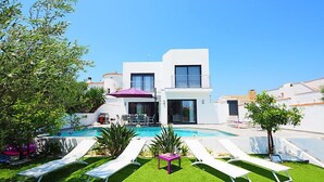 Una villa moderna con piscina, tumbonas y un césped bien cuidado.