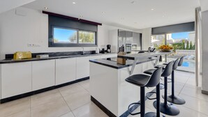 Una cocina moderna con una isla central, taburetes de bar y vistas a una piscina.